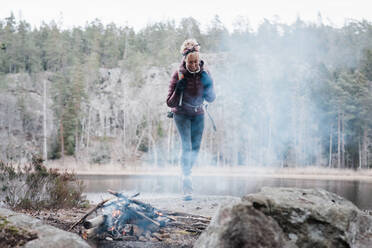 Frau, die auf einem Felsen in Richtung eines Lagerfeuers an einem See in Schweden läuft - CAVF84985