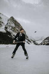 Eishockeyspieler im Anzug jongliert Puck auf zugefrorenem See in den Bergen - CAVF85021