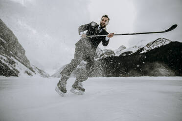 Lächelnder Eishockeyspieler im Anzug hält schnell auf dem zugefrorenen Lake Louise an - CAVF85023