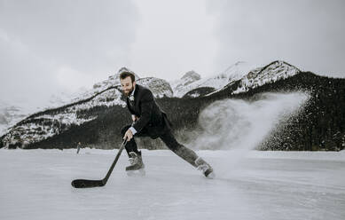 Eishockeyspieler im Anzug hält schnell an und schießt gefrorene Gischt auf den See - CAVF85025