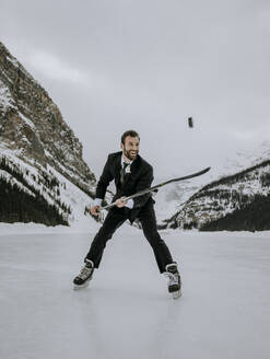 Mann in Anzug und Schlittschuhen jongliert Eishockey-Puck auf dem gefrorenen Lake Louise - CAVF85026