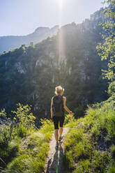 Woman with backpack hiking on mountain trail during sunny day, Lecco, Italy - MCVF00433