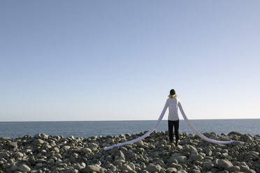 Frau mit künstlichen langen Händen steht auf Kieselsteinen am Strand gegen klaren Himmel - PSTF00758