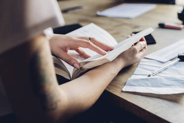 Close-up of woman reading book at table in office - MEUF00651