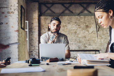 Portrait of creative business man sitting at table in loft office - MEUF00652