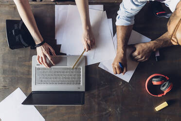 Zwei kreative Geschäftsleute arbeiten mit Laptop und Papieren auf einem Holztisch - MEUF00675