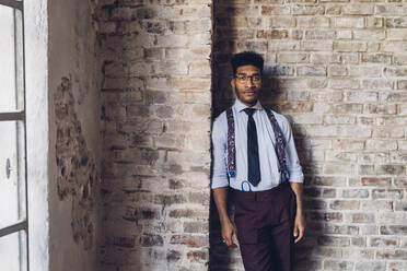 Portrait of a stylish young man standing at brick wall in loft - MEUF00678