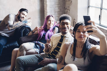 Group of friends sitting on sofa in a lofttaking a selfie - MEUF00702