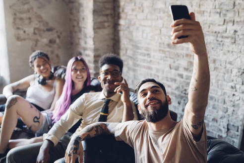 Gruppe von Freunden sitzt auf dem Sofa in einem Loft und macht ein Selfie - MEUF00706