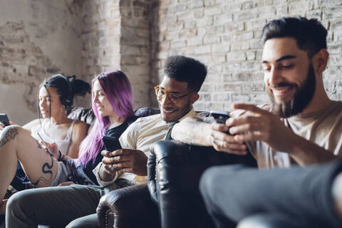 Gruppe von Freunden sitzt auf dem Sofa in einem Loft und benutzt Smartphones, lizenzfreies Stockfoto