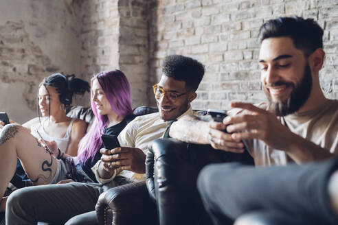 Gruppe von Freunden sitzt auf dem Sofa in einem Loft und benutzt Smartphones - MEUF00707