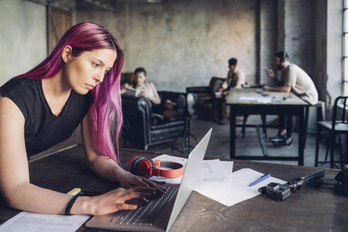 Kreative Geschäftsfrau mit rosa Haaren, die einen Laptop in einem Loft-Büro benutzt - MEUF00732