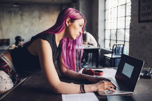 Kreative Geschäftsfrau mit rosa Haaren, die einen Laptop in einem Loft-Büro benutzt - MEUF00738