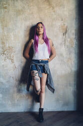 Porträt einer stilvollen jungen Frau mit rosa Haaren, die an einer Wand lehnt - MEUF00748