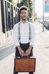 Portrait of a confident stylish young businessman holding briefcase in the city - MEUF00763