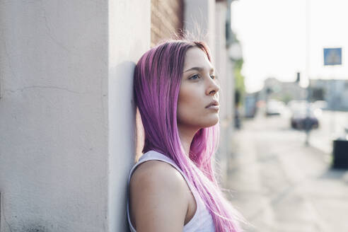 Porträt einer stilvollen jungen Frau mit rosa Haaren, die sich in der Stadt an eine Wand lehnt - MEUF00779