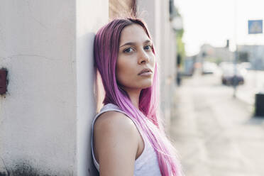 Porträt einer stilvollen jungen Frau mit rosa Haaren, die sich in der Stadt an eine Wand lehnt - MEUF00780