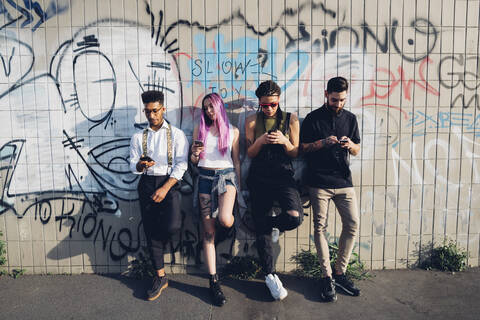 Group of friends using smartphones at a graffiti wall in the city stock photo