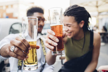 Glückliches junges Paar stößt im Freien an einer Bar mit Biergläsern an - MEUF00806