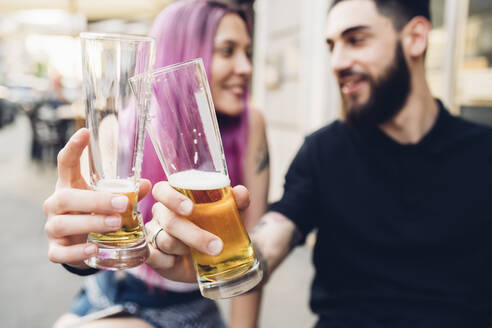 Glückliches junges Paar stößt im Freien an einer Bar mit Biergläsern an - MEUF00807