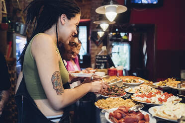 Glückliche Freunde nehmen Essen vom Buffet in einem Restaurant - MEUF00808