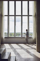 Senior man looking out of window in a loft flat - MCF00913