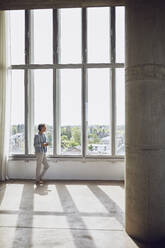 Senior man looking out of window in a loft flat - MCF00914