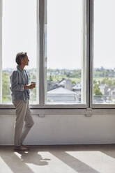 Älterer Mann schaut aus dem Fenster in einer Dachgeschosswohnung - MCF00918