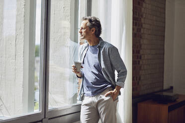 Senior man looking out of window in a loft flat - MCF00921