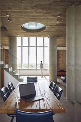 Laptop on wooden table in a loft flat with man at the window in background - MCF00935