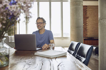 Senior man sitting at the table in a loft flat using laptop - MCF00942