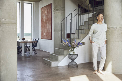 Senior man leaning against a column in a loft flat - MCF00949