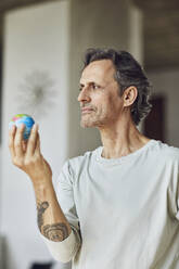 Älterer Mann hält Mini-Globus in einer Dachgeschosswohnung - MCF00960