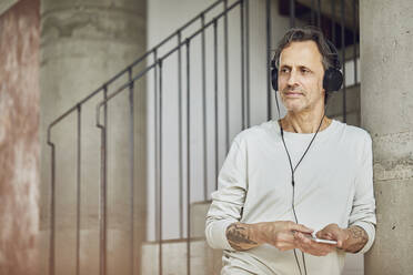 Senior man with headphones listening music in a loft flat - MCF00963