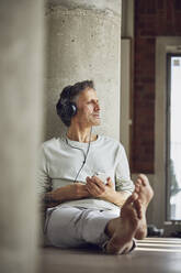 Älterer Mann mit Kopfhörern, der in einer Loftwohnung Musik hört - MCF00979
