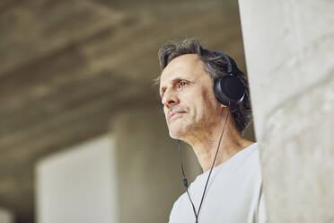 Älterer Mann mit Kopfhörern, der in einer Loftwohnung Musik hört - MCF00982