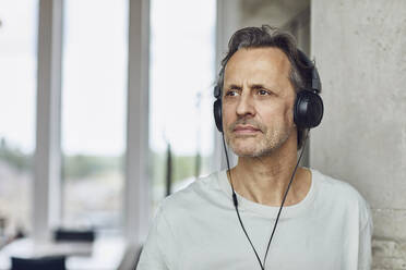 Senior man with headphones listening music in a loft flat - MCF00990