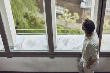 Älterer Mann schaut aus dem Fenster in einer Dachgeschosswohnung - MCF01004