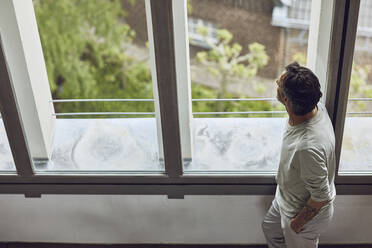 Senior man looking out of window in a loft flat - MCF01004