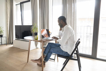 Mann sitzt am Tisch in einer modernen Wohnung und benutzt einen Laptop - AHSF02732