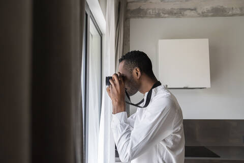 Mann fotografiert mit Kamera aus dem Fenster zu Hause, lizenzfreies Stockfoto