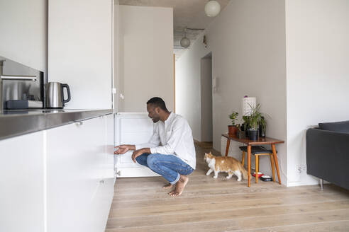 Man crouching in the kitchen looking into freezer - AHSF02757