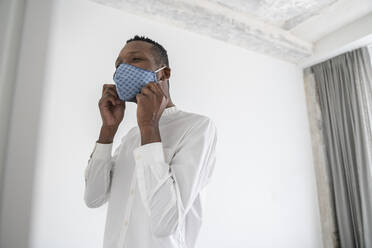 Man putting on reusable face mask indoors - AHSF02761