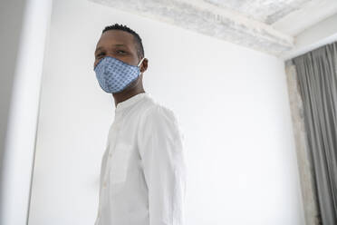Portrait of man wearing reusable face mask indoors - AHSF02762
