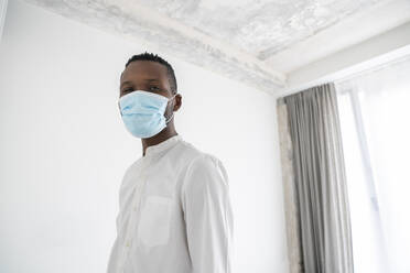 Portrait of man wearing disposable face mask indoors - AHSF02764