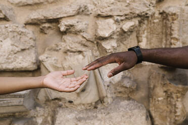 Cropped hands of couple reaching each other against stone wall - EGAF00177