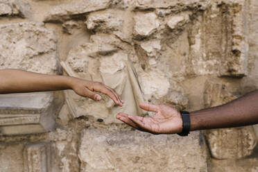 Hands of couple reaching each other against stone wall - EGAF00178