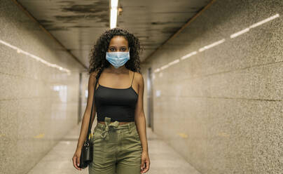 Frau trägt Masken, während sie in einem unterirdischen Gang einer U-Bahn-Station steht - EGAF00196