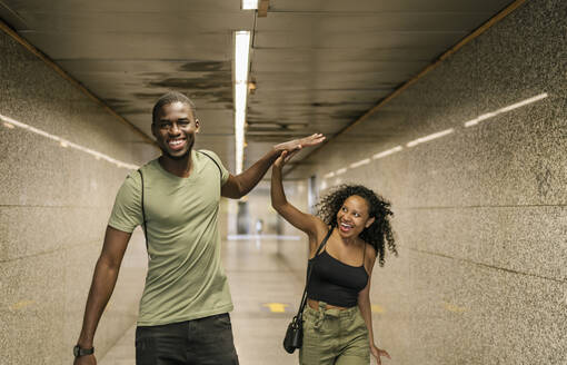 Fröhliches Paar gibt sich beim Gehen im unterirdischen Gang einer U-Bahn-Station die Hand - EGAF00198