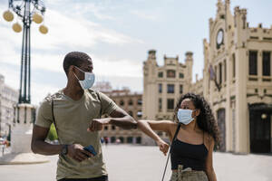 Man and woman wearing masks while greeting each other with elbows in city - EGAF00201